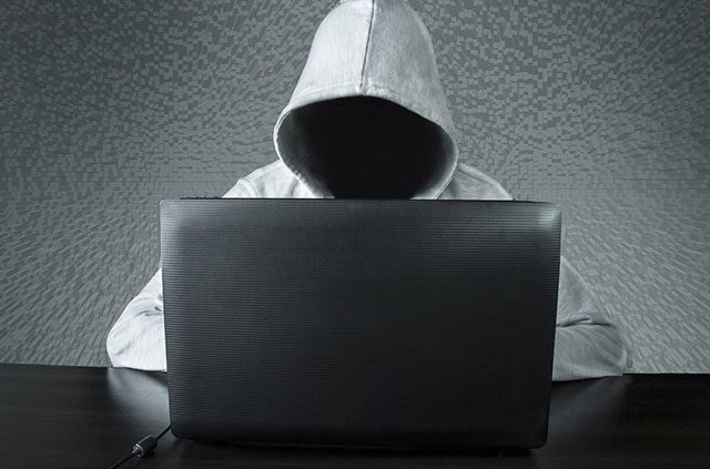 A person in a hoodie, wit their face obscured, using a laptop.